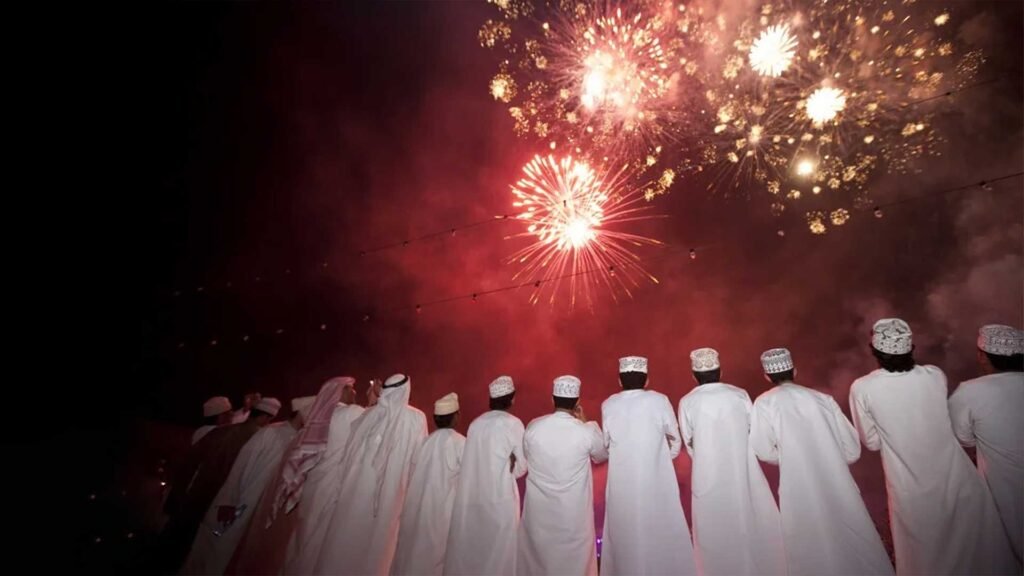 A group of people dressed in traditional Omani attire watching a fireworks display during a nighttime celebration, reflecting Oman cultural etiquette and traditions.