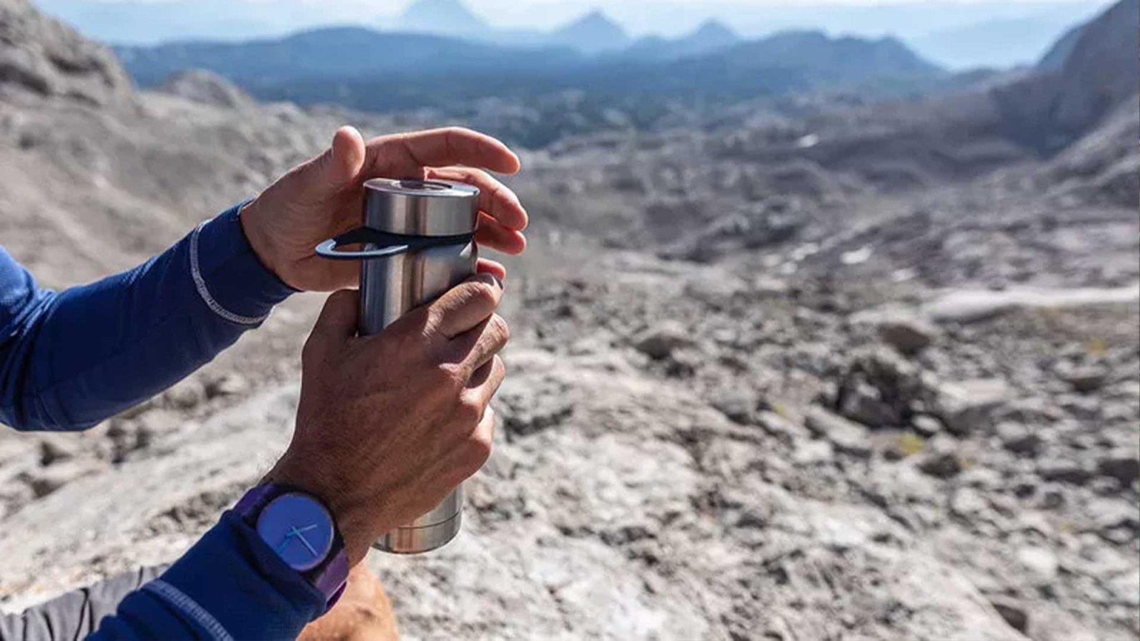 Close-up of a traveler holding a water bottle while exploring rocky terrain, emphasizing the need for hydration in an Oman travel packing list.