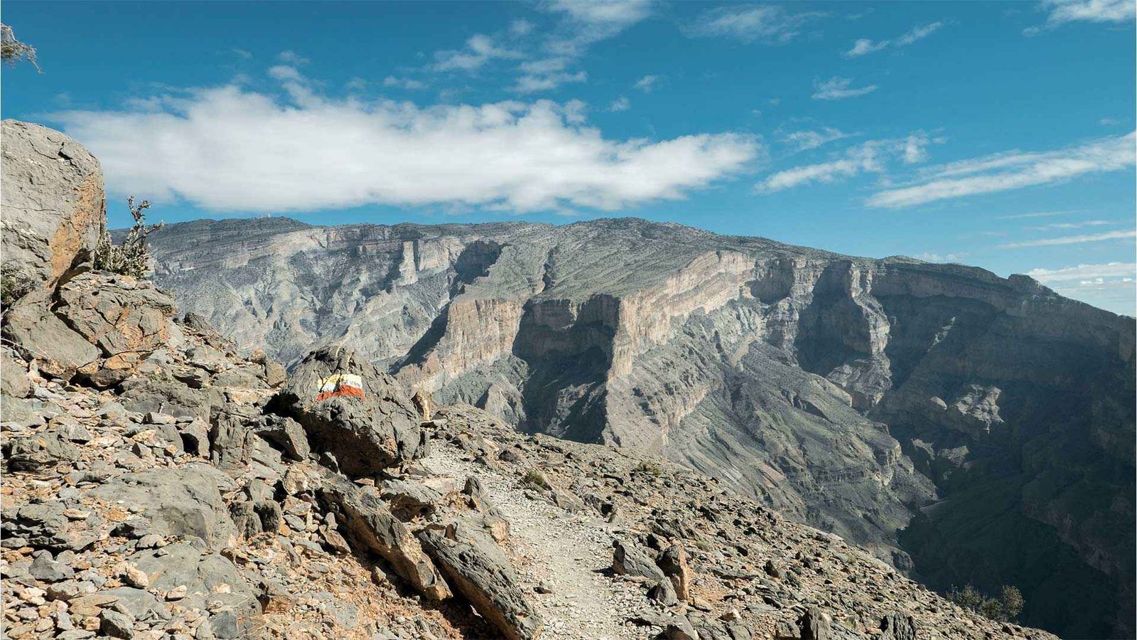 A breathtaking view of Jebel Shams, Oman's highest peak, showcasing rugged rocky cliffs and a clear blue sky.