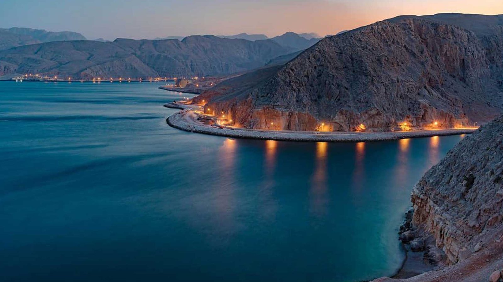 Stunning view of the Musandam Peninsula at dusk, with rugged mountains meeting the calm blue waters, highlighting one of the breathtaking Oman tourist attractions.