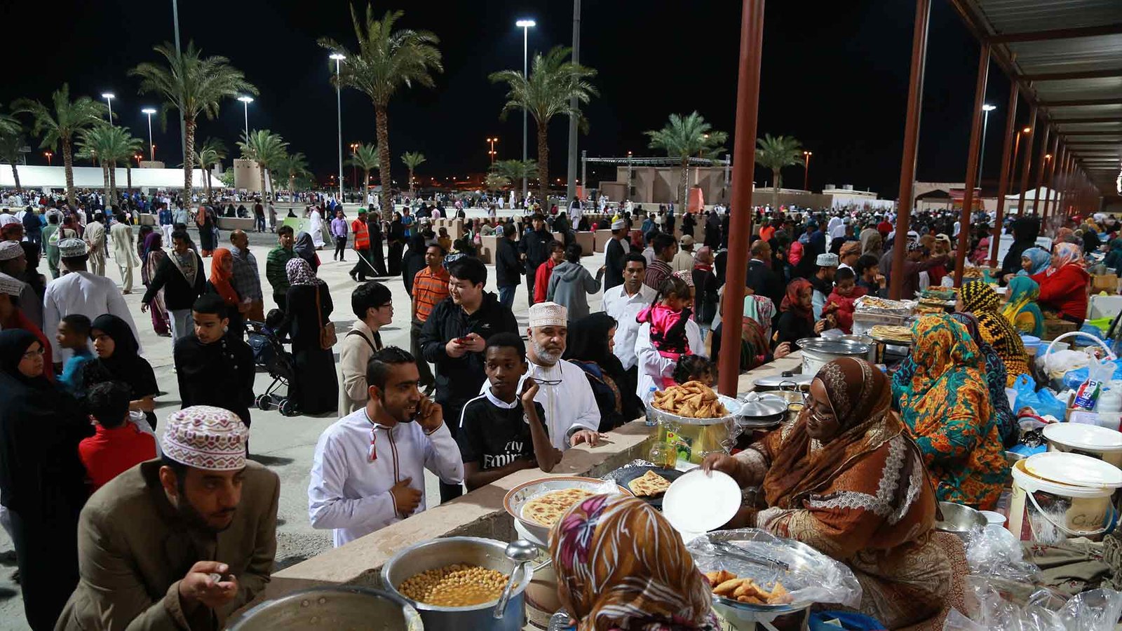 A bustling night market scene at one of the Omani festivals and events, where crowds of people enjoy traditional Omani dishes served by vendors. The vibrant atmosphere showcases the rich culinary heritage of Oman during the Oman International Food Festival.