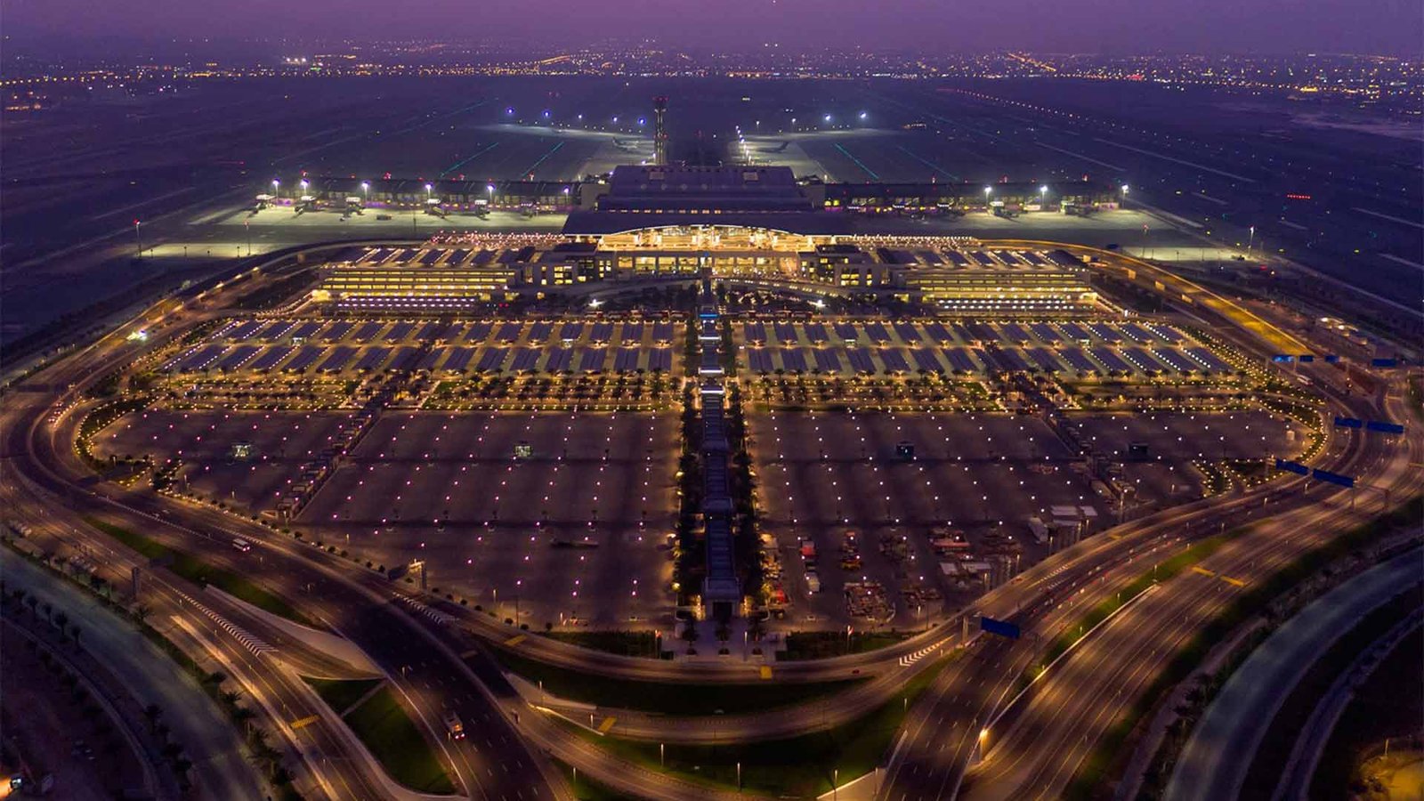 Aerial view of Muscat International Airport at night, showcasing the vast parking area, well-lit roads, and the airport terminal. The image highlights the infrastructure related to Oman visa requirements and entry into the country.