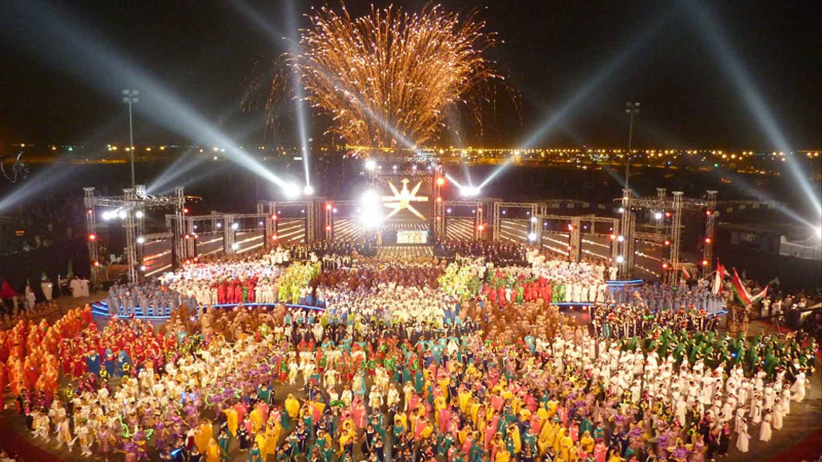 A vibrant and colorful celebration at night with large crowds dressed in traditional attire, gathered under a spectacular display of fireworks and lights during one of the major Omani festivals and events. This image captures the grandeur and unity of Oman’s cultural festivities.