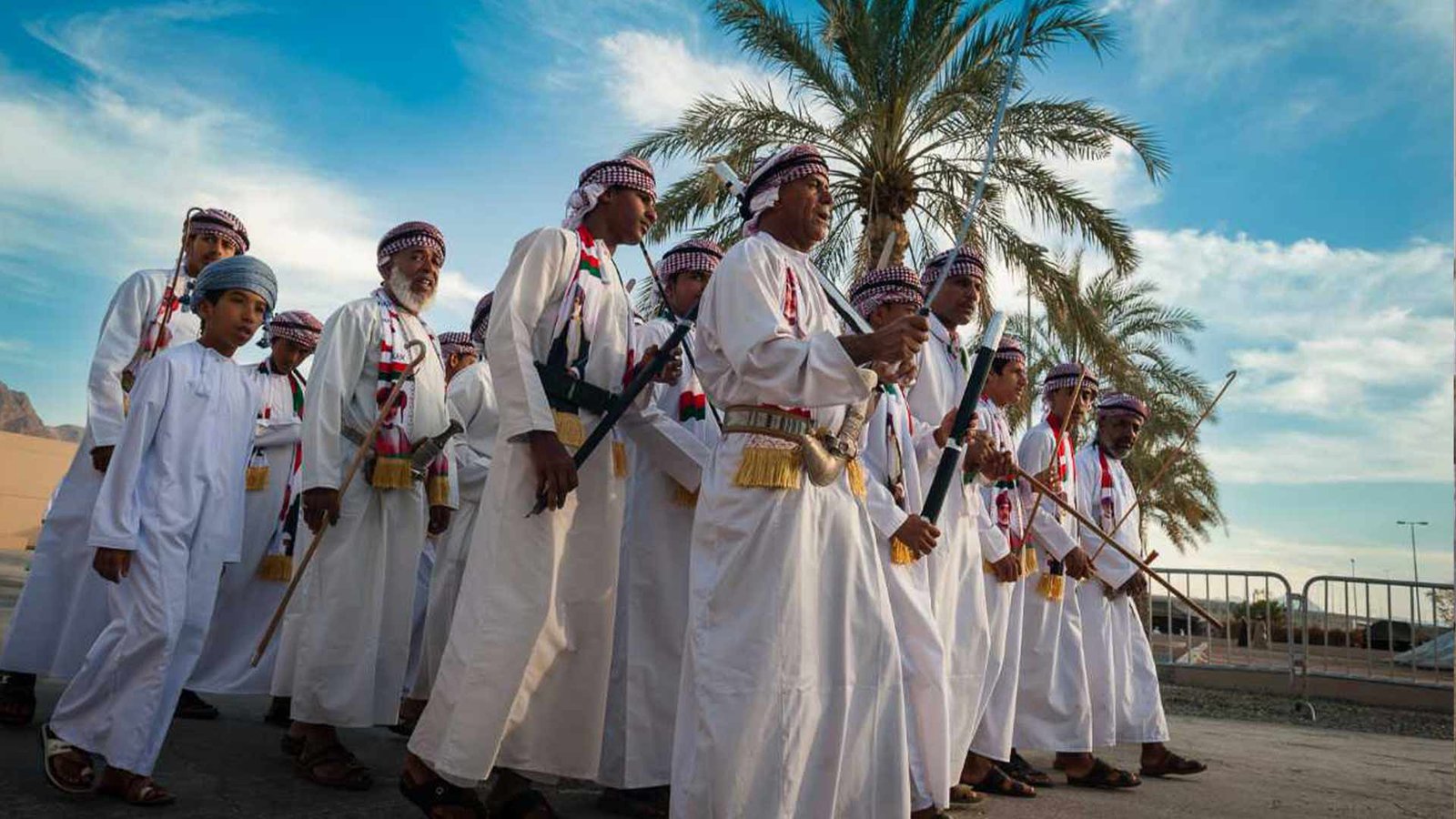 Group of Omani men and boys dressed in traditional attire performing a cultural dance with rifles, highlighting Oman cultural etiquette and traditions in music and dance.