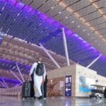 A traveler walks through a modern, spacious terminal at an Omani airport, surrounded by purple-lit ceilings and clear signage pointing to check-in zones. The scene highlights the well-organized and welcoming atmosphere for those navigating Oman airport transportation guide.