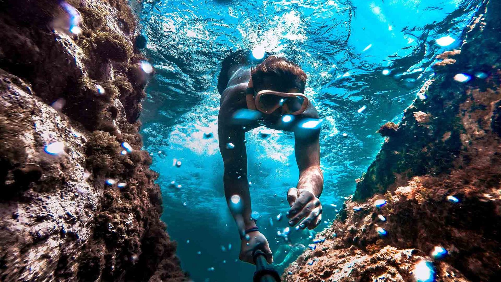 A snorkeler exploring a vibrant underwater scene, navigating between rocky formations with clear blue water all around, showcasing the excitement of Scuba Diving and Snorkeling Spots Oman.